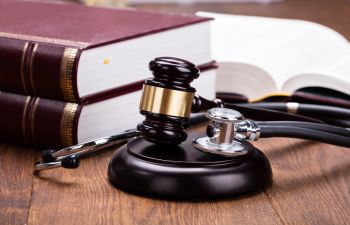 A gavel and stethoscope rest on a wooden desk beside law books, suggesting a connection between legal and medical fields.