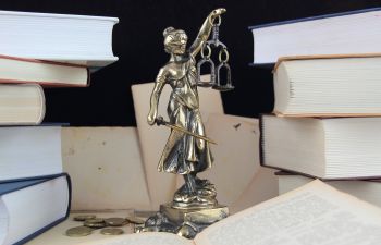 A statue of Lady Justice holding scales and a sword, surrounded by open and closed books.