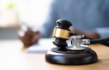 A gavel and a stethoscope on a desk of a medical malpractice lawyer revising documents.