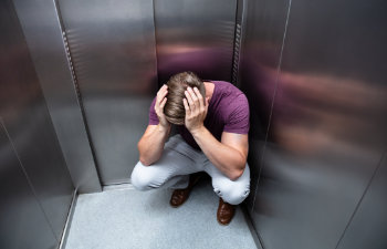 Crouched Worried Man With Hands On Head In Elevator