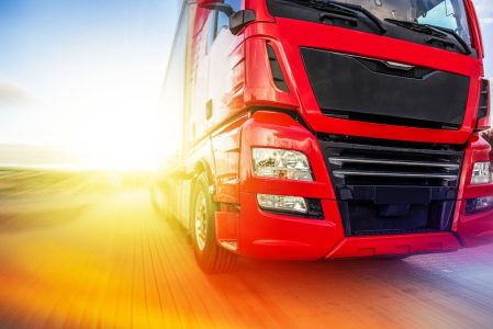 Red truck driving on a road with a bright sun in the background.