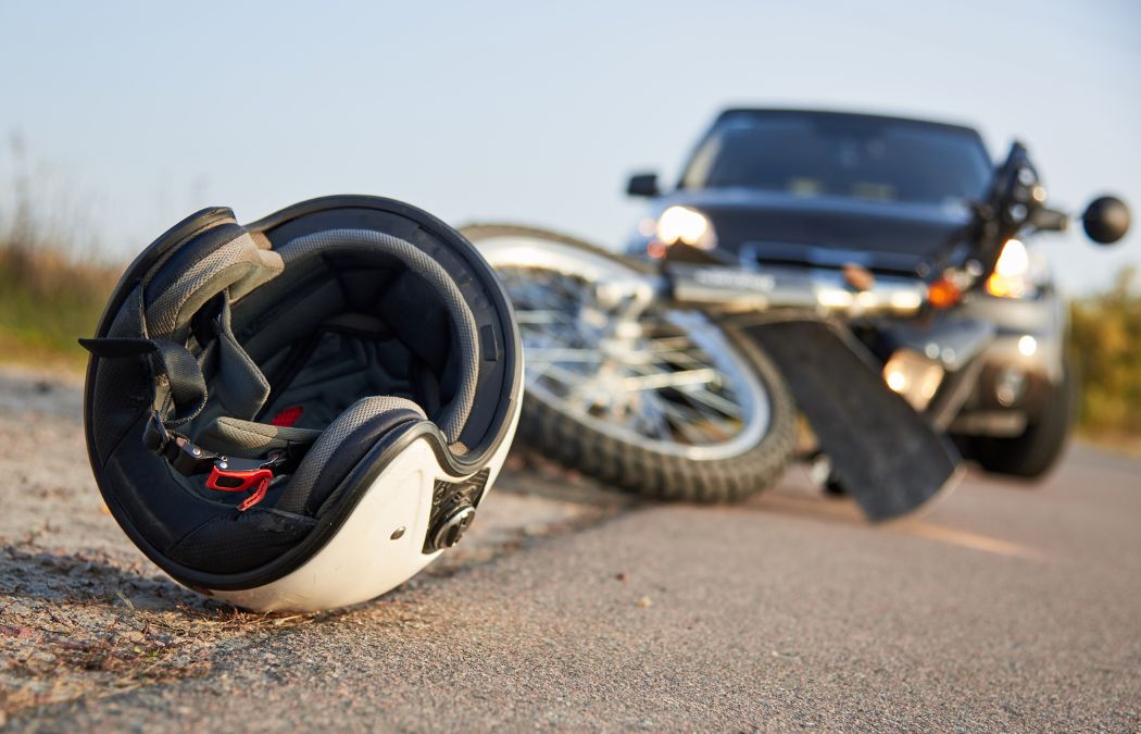 A motorcycle and helmet lie on the road in front of a car, suggesting a collision.