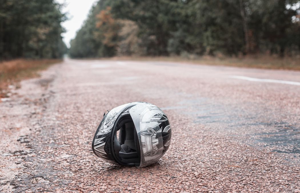 Motorcycle helmet lying on an empty, paved road with trees in the background.