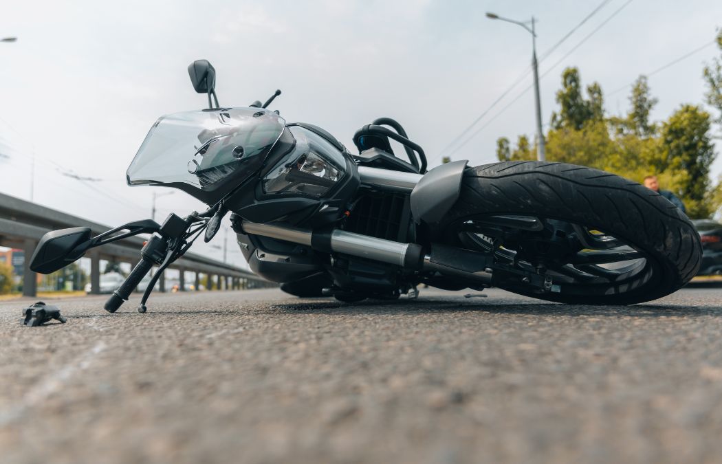 A black motorcycle lies on its side on a paved road.
