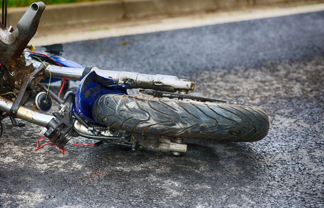 Fallen motorcycle on an asphalt road with visible damage to the frame and detached front wheel.