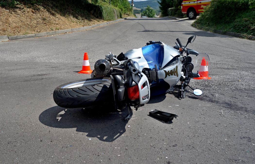 Motorcycle lying on its side on the road beside traffic cones, with scattered debris nearby.