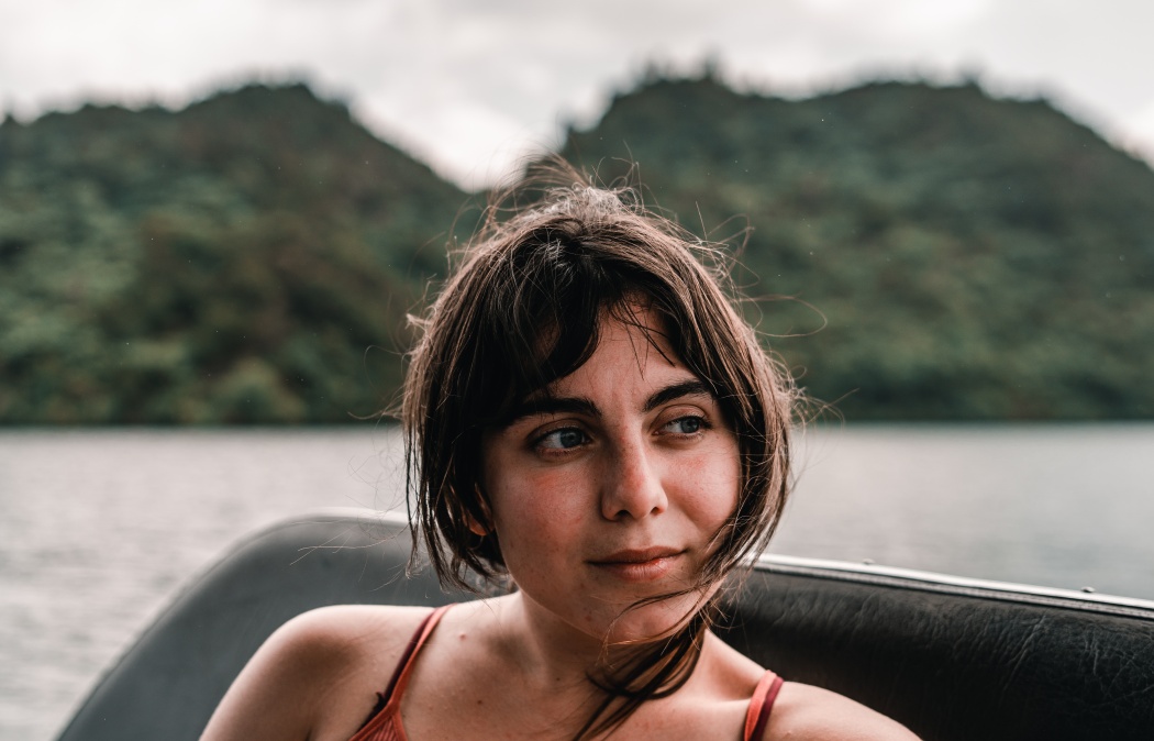 head and face of a disheveled blue eyed caucasian young woman smiling calm and relaxed from a boat sailing on the lake, tarawera lake, new zealand